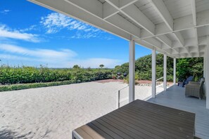 A covered outdoor area with a sandy beach, a wooden deck, and a seating area with chairs. - "SALT WIND" HAS GULF VIEWS, STEPS TO BEACH, SECLUDED & PEACEFUL! (Mexico Beach)