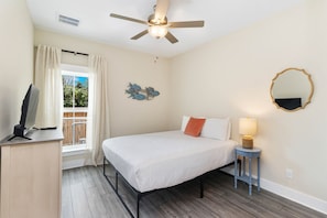 A bedroom with a bed, a ceiling fan, a window with curtains, a wall-mounted mirror, and a bedside table with a lamp. - Salty Blue is a new 2BD/2BA cottage, walking distance to restaurants & shops! Po (Port Saint Joe)