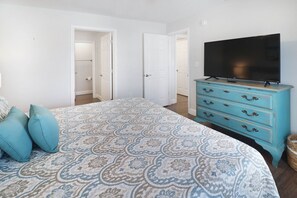 A bedroom with a patterned bedspread, a blue dresser with a television, and two white doors. - "Sandals and Sunsets" located in a gulf front community! Steps to paradise! Pet (Mexico Beach)