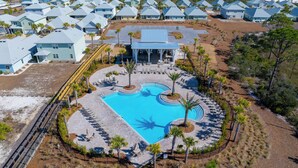 Eine Luftaufnahme eines Resorts mit einem zentralen Schwimmbecken, umgeben von Liegebereichen und Palmen.