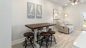 Ein Essbereich mit einem Holztisch, vier Hockern, einem grauen Sofa und Kunstwerken an den Wänden.