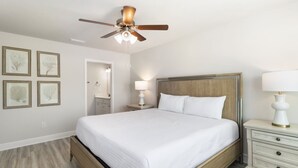 Ein Hotelzimmer mit Bett, Nachttisch, Deckenventilator, Nachttischlampe und gerahmten Kunstwerken an der Wand.
