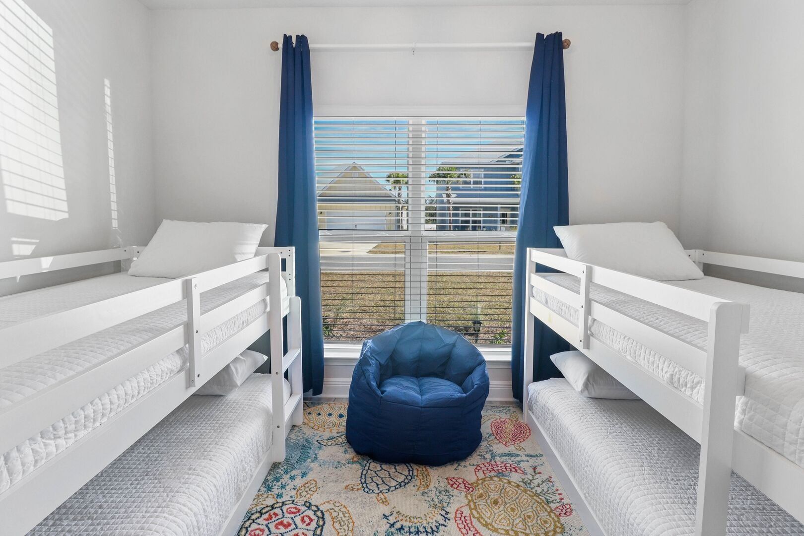 A room with two bunk beds, a blue bean bag chair, and a patterned rug.