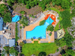 Ett flygbildsbild av ett semesterområde med en stor swimmingpool, solstolar och ett överbyggt område.