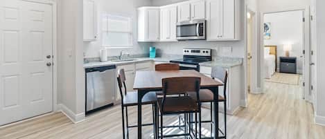 Une cuisine moderne avec des armoires blanches, un lave-vaisselle en acier inoxydable, un four à micro-ondes et une cuisinière. On y trouve une table à manger avec quatre chaises.