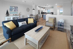 A modern living room with a sofa, coffee table, and a view into the kitchen. - SEABISCUIT IS 325 STEPS TO BEACH & GULF VIEWS GALORE! 3BD LUXURY TOWNHOME! (Mexico Beach)