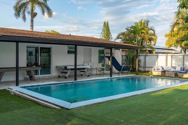 Une maison moderne dotée d’une piscine, d’un espace salon extérieur et d’un patio couvert.