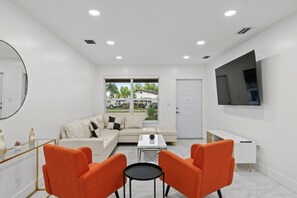 Un salon moderne comprenant un canapé, deux fauteuils, une table basse et un téléviseur fixé au mur.