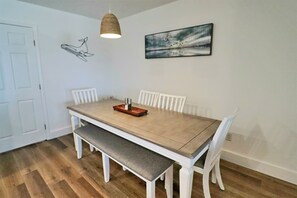 A dining area with a wooden table, white chairs, a bench, a hanging light fixture, and a wall-mounted artwork. - "SEA-CHELE" IS A BEAUTIFULLY DECORATED 2BD TOWNHOUSE JUST STEPS TO THE BEACH! (Mexico Beach)
