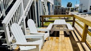Eine Holzterrasse mit weißen Adirondack-Stühlen und einem Picknicktisch.