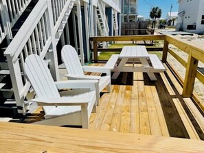 En träveranda med vita Adirondack-stolar och ett picknickbord.