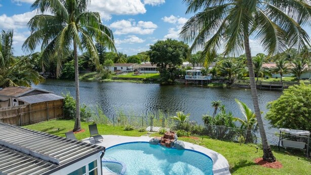 Patio con piscina, rodeado de palmeras y vista a un lago.