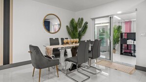 Un comedor moderno con una mesa de vidrio, sillas tapizadas en gris y un espejo decorativo.