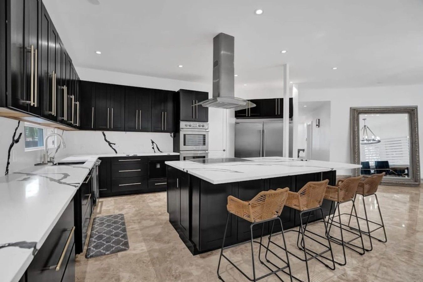 A modern kitchen with a central island, black cabinetry, stainless steel appliances, and a bar area with wicker chairs.