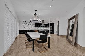 A modern dining area with a marble floor, a white table, black chairs, and a chandelier. - Luxury Mansion | 5K SF | Pool & Game Room (Hollywood)