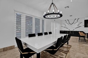 A modern dining area with a long white table, black chairs, and a chandelier. - Luxury Mansion | 5K SF | Pool & Game Room (Hollywood)