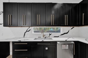 A modern kitchen with black cabinets, a white countertop, and a window above the sink. - Luxury Mansion | 5K SF | Pool & Game Room (Hollywood)