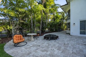 A patio area with a swing chair, round table, and rectangular seating. - Luxury Mansion | 5K SF | Pool & Game Room (Hollywood)