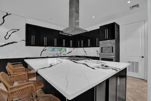 A modern kitchen with a large island, dark cabinetry, and a stainless steel range hood. - Luxury Mansion | 5K SF | Pool & Game Room (Hollywood)