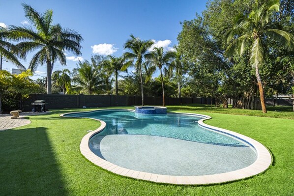 A swimming pool with a curved design, surrounded by well-maintained grass and palm trees. - Luxury Mansion | 5K SF | Pool & Game Room (Hollywood)