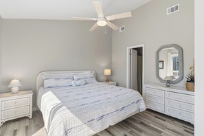 Une chambre à coucher comprenant un lit, des tables de chevet, une commode, un ventilateur de plafond et un miroir.