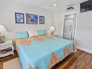 Ein Schlafzimmer mit einem Bett, zwei Nachttischen, einem Beistelltisch, einer Tür und drei gerahmten Bildern an der Wand.