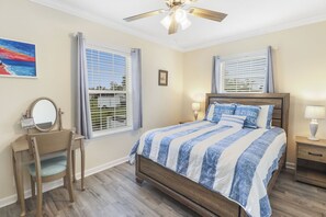 A bedroom with a bed, a vanity with a mirror, two windows with blinds, a ceiling fan, and a nightstand with a lamp. - SERENITY ON SEA STREET IS 650 FT TO BEACH! SCREENED PORCH, FENCED-IN YARD! (Mexico Beach)