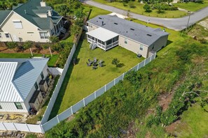 An aerial view of a residential area with a large house featuring a spacious lawn, a covered patio, and a fenced yard. - SERENITY ON SEA STREET IS 650 FT TO BEACH! SCREENED PORCH, FENCED-IN YARD! (Mexico Beach)