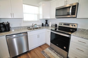 A modern kitchen with stainless steel appliances, white cabinetry, and a granite countertop. - SHORE BEATS WORK IS 500 STEPS TO BEACH! MODERN, IMMACULATE TOWNHOME! (Mexico Beach)