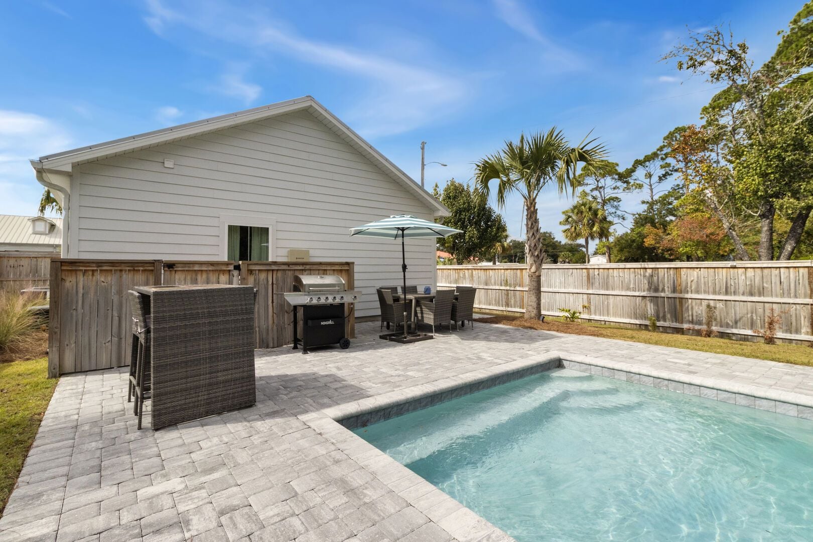 A backyard with a swimming pool, a barbecue grill, and outdoor furniture.