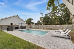 Ein Garten mit Schwimmbad, Grillplatz und Liegestühlen.