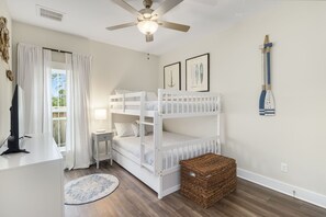 Ein Schlafzimmer mit Etagenbetten, einem Schreibtisch, einer Lampe, einem Deckenventilator und einem Fenster mit Vorhängen.