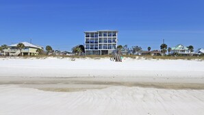 Ein Hotel direkt am Strand mit mehreren Stockwerken, einem sandigen Strand im Vordergrund und einem klaren, blauen Himmel.