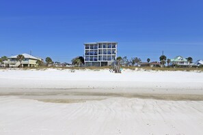 Ett hotell vid stranden med flera våningar, en sandstrand i förgrunden och en klarblå himmel.