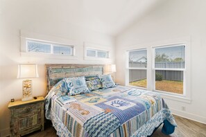 Un dormitorio con una cama grande, una mesita de noche, una lámpara y vistas al exterior a través de una ventana.