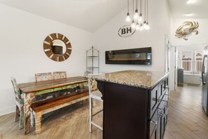 Una cocina moderna con una isla central, una mesa de comedor con sillas, un espejo redondo y un televisor montado.
