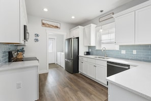 A modern kitchen with white cabinetry, a stainless steel refrigerator, and a built-in dishwasher. - NEW LISTING! Special Sunset is steps to beach, hot tub, fenced backyard and pet (Mexico Beach)