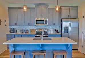 Una cocina moderna con gabinetes grises, electrodomésticos de acero inoxidable y una isla central con taburetes.
