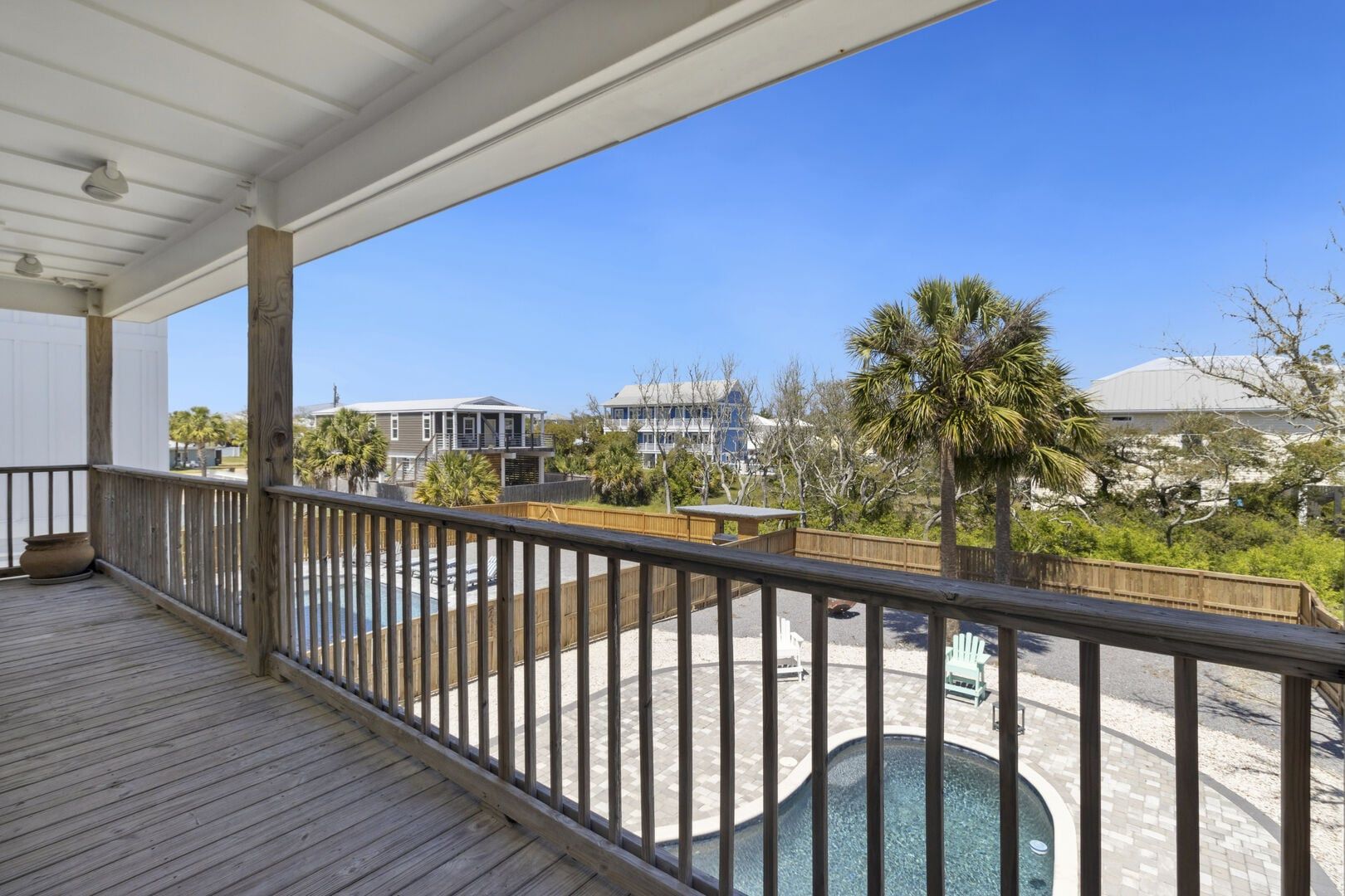 A wooden deck with a pool, surrounded by a wooden fence and palm trees.