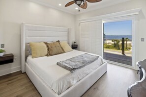 Ein Schlafzimmer mit einem großen Bett, einem Deckenventilator, einem Nachttisch und Blick auf den Strand durch eine Schiebetür.