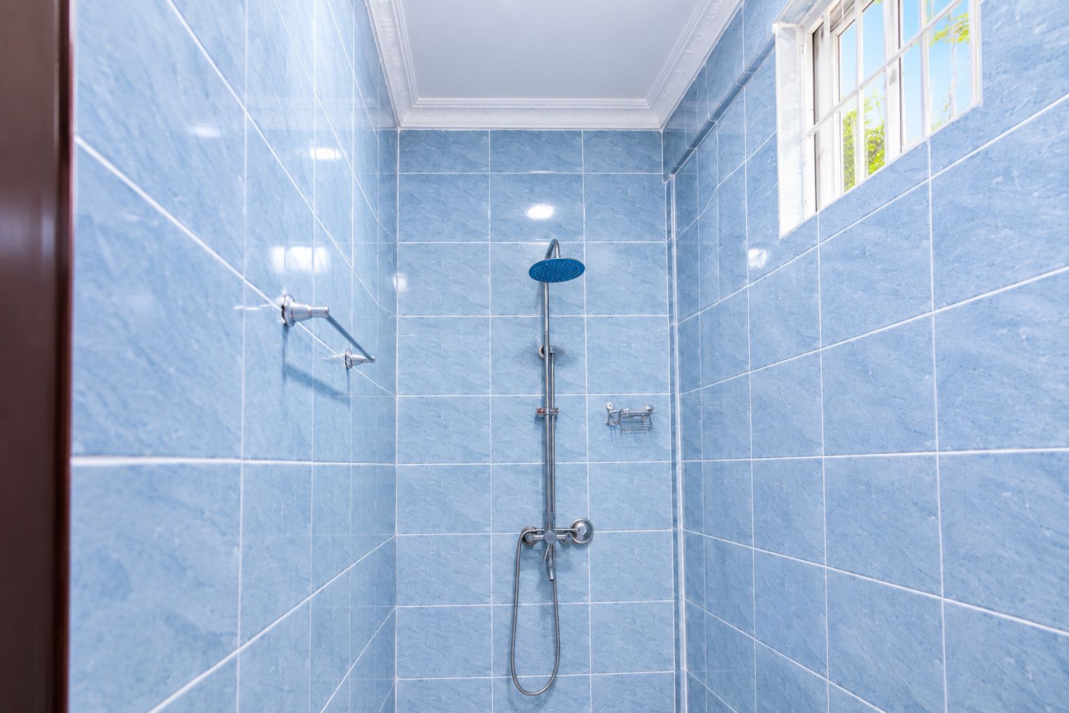 Casa de banho com paredes revestidas a azulejos azuis, um chuveiro e um pulverizador manual.
