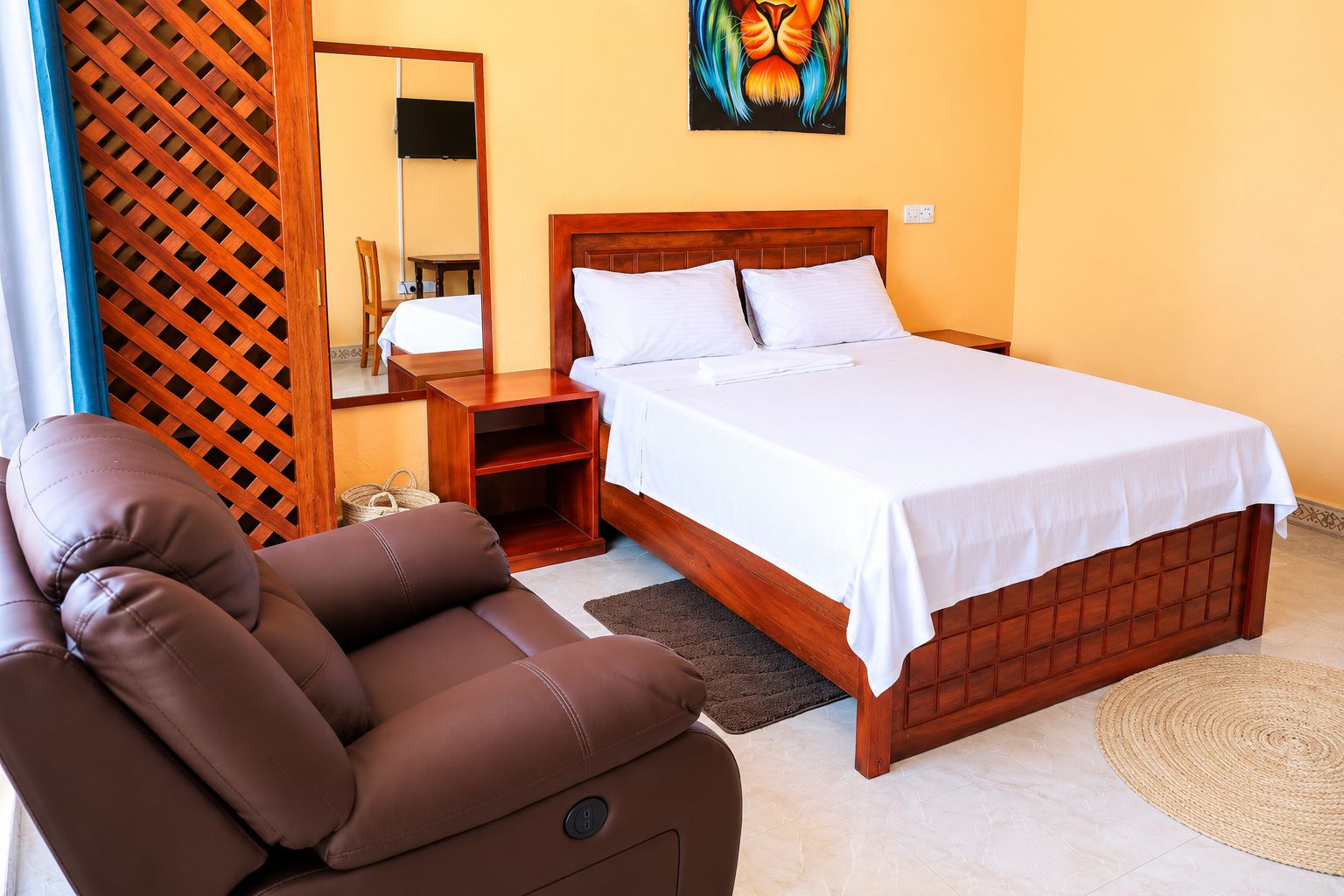 A bedroom with a wooden bed, a brown leather chair, a bedside table, and a wall-mounted TV.