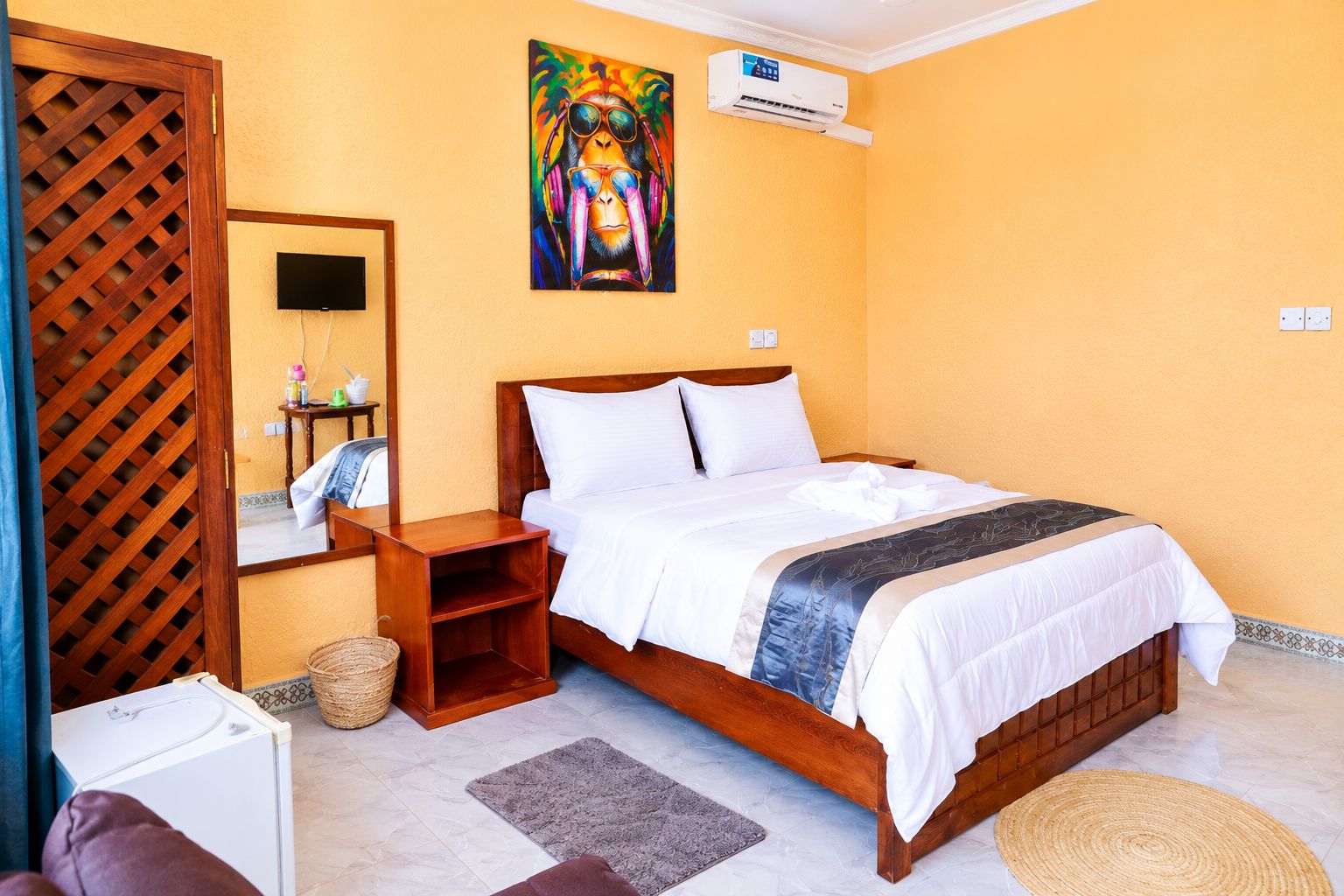 A hotel room with a bed, a wooden nightstand, a television, and a wall-mounted air conditioner.