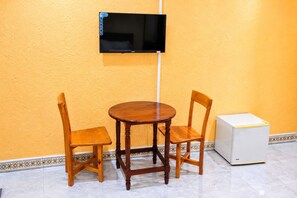 A room with a wooden table and two chairs, a television mounted on the wall, and a white appliance on the floor.