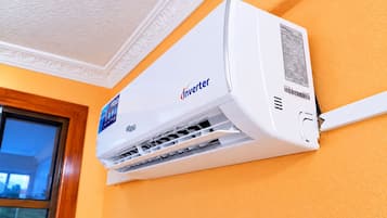 Un equipo de aire acondicionado Inverter montado en una pared con una ventana a la izquierda.