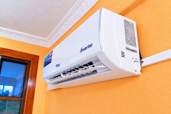 An Inverter air conditioning unit mounted on a wall with a window to the left.