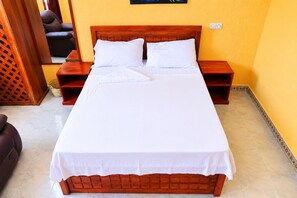 A neatly made bed with white linens and a wooden headboard in a room with yellow walls and a tiled floor.