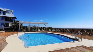 Une piscine avec une terrasse en bois, un espace salon couvert et une vue sur l’océan.