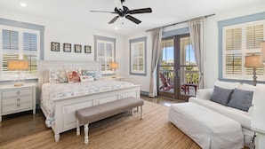 Une chambre à coucher comprenant un lit, un banc, un canapé, un ventilateur de plafond et une vue sur l’extérieur, visible à travers une porte vitrée.