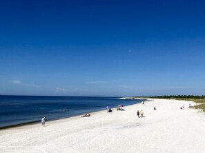 Ein Strand mit weißem Sand, klarem, blauem Wasser und ein paar Personen.